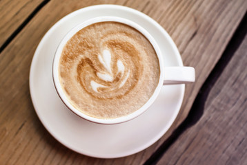 Art cappuccino in the white cup on the wooden surface.Top view photography.The beauty of minimalism.Warm toned photo.