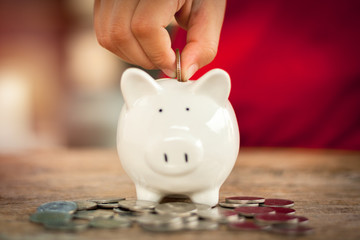 Small hand putting coin in piggy bank some coins on wooden table. Save money concept for education and suport in the future.