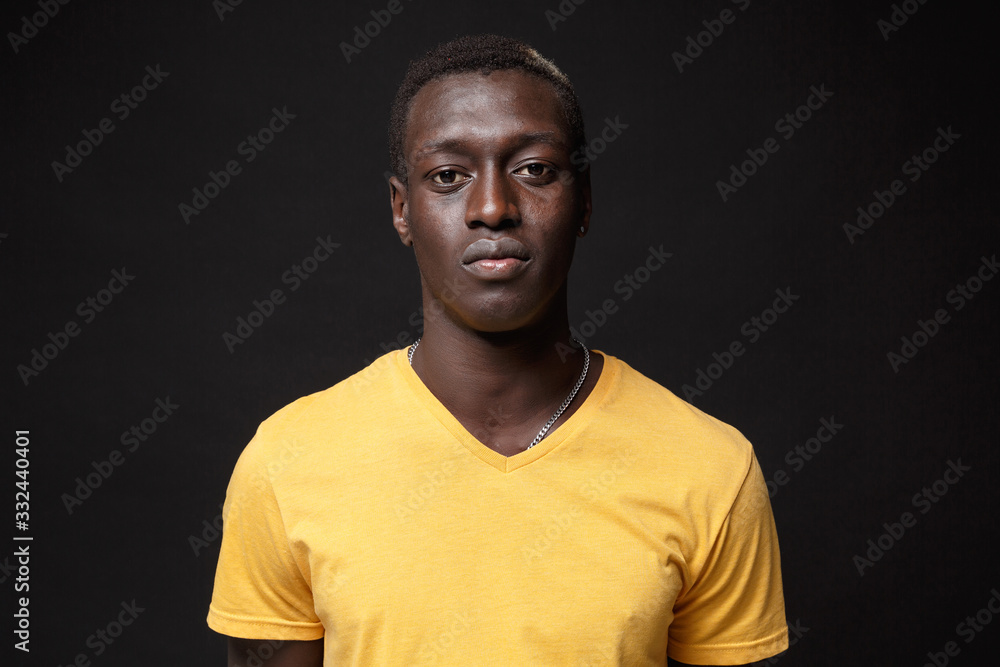 Handsome young african american man guy in yellow t-shirt posing isolated on black wall background studio portrait. People sincere emotions, lifestyle concept. Mock up copy space. Looking camera. - obrazy, fototapety, plakaty 