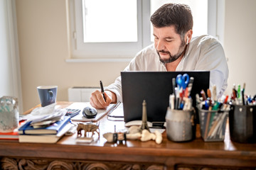 man with earphones having conference call online sitting at home office with laptop. working from ho