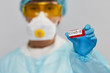 © veles_studio - test tube with COVID-19 in the arm of professional biochemist wearing protactive costume of mask glasses hat and gloves