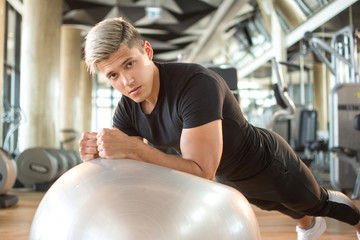 Handsome young man doing plank exercise on fitness ball at gym