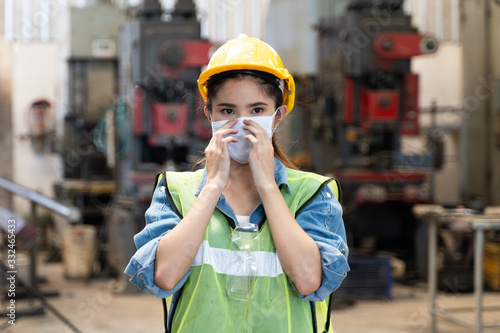 Asian women worker factory wearing mask protection face for safety stands in machine industrial factory.