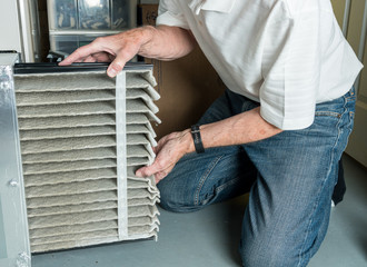 Wall Mural - Senior caucasian man changing a folded dirty air filter in the HVAC furnace system in basement of home