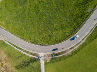 Canvas Print - Aerial view of sharp hairpin curve of road through green meadow. Concept of traveling by car.