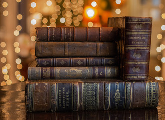 A vintage pile of three old brown leather books with eye glasses on a wood table.