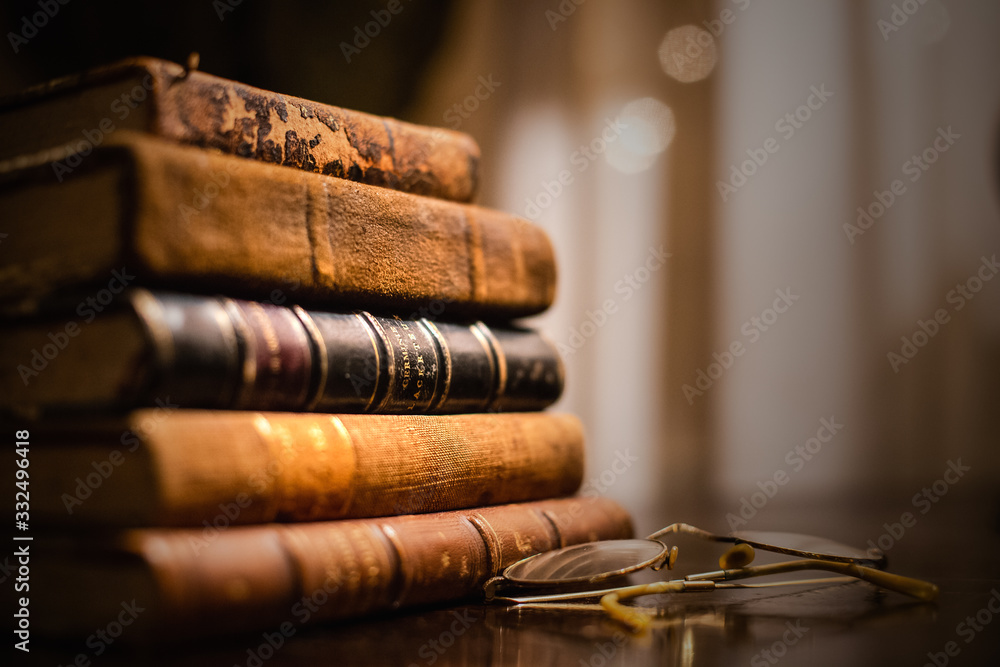 A vintage pile of five old brown leather books with eye glasses on a wood table. - obrazy, fototapety, plakaty 