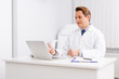 © LIGHTFIELD STUDIOS - handsome otolaryngologist having video chat on laptop while sitting at workplace