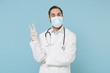 © ViDi Studio - Cheerful male doctor man in white medical gown sterile face mask gloves isolated on blue wall background. Epidemic pandemic coronavirus 2019-ncov sars covid-19 flu virus concept. Showing victory sign.