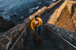 © Ekaitz Gerique/ADDICTIVE STOCK - High angle of male in bright yellow jacket with big brown dog walking up stone stairs and looking away with interest against troubled bay water washing rocky coast in Spain during sunrise