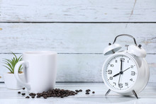 White Retro Alarm Clock, Flowers Cup Of Coffee , Coffee Beans And Cinnamon On A Wooden Table. Breakfast Coffee. Morning. Espresso	