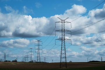 Field with electric poles and a beautiful blue sky with clouds highlighted by the sun