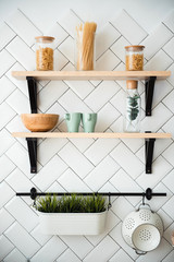 Wall Mural - Kitchen utensils, pot plant and glass jars with pasta on wooden shelves. White tile on background. Kitchen details