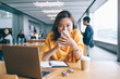 © BullRun - Female shop assistant covering face with smartphone on coffee break in electronic store