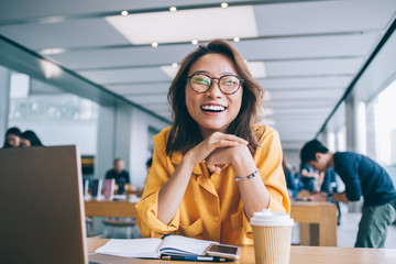 Portrait of excited hipster student in classic glasses for vision protection feeling excited and laughing during free time in university classroom, happy smiling Chinese woman e learning indoors