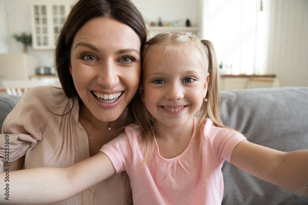 Smiling young mother and small preschooler daughter look at camera making selfie at home together, happy funny mom and little girl child have fun laugh take photo posing for self-portrait picture - obrazy, fototapety, plakaty 