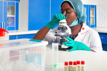 African female medical student, woman scientist In protective white gown, plastic hat, gloves, mask works with microscope in laboratory, test lab. Analysis of histology samples of patients biopsy.