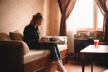 Wall Mural - Young woman using typewriter while sitting on sofa at home