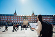 © eldarnurkovic - Visiting famous landmarks and places.Cheerful female traveler at famous Plaza Mayor square reading a map. Marid,Spain travel experience. Backpacker, travel photography.