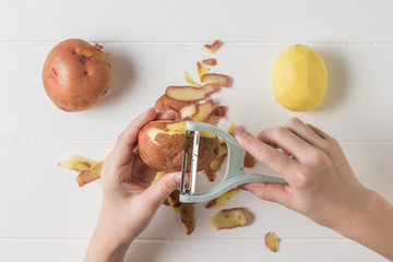 The child peels potatoes with a special knife.