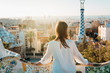 Young female tourist spending vacation in Barcelona,Catalonia,Spain.Traveling to Europe,visiting Parc Guell UNESCO site famous historical landmarks.Panoramic view on entrance.Best sunrise in Barcelona