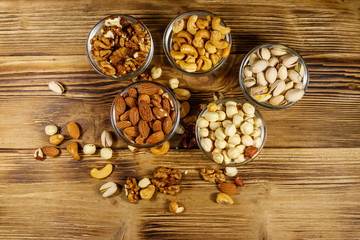 Sticker - Assortment of nuts on wooden table. Almond, hazelnut, pistachio, walnut and cashew in glass bowls. Top view. Healthy eating concept