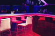 Glass of bright green neon cocktail on a bar table in night club blue and red lights. Party or nightlife entertainment with copy space