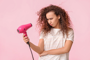 Wall Mural - Frowning young woman with blow dryer on color background