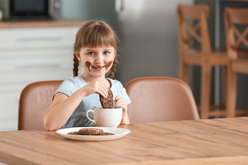 Wall Mural - Cute little girl eating melted chocolate and cookies in kitchen