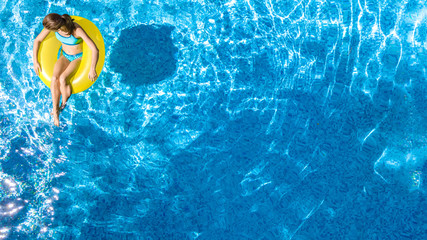 Active young girl in swimming pool aerial top view from above, child relaxes and swims on inflatable ring donut and has fun in water on family vacation, tropical holiday resort