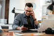 © JustLife - Businessman in office. Handsome man using phone at work.