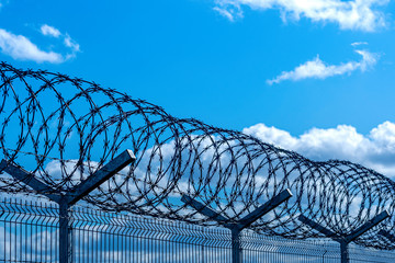 fence with barbed wire against blue sky with clouds