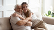 © fizkes - Portrait happy older father and adult daughter hugging, looking at camera, posing for photo, beautiful young woman with smiling mature dad or grandfather sitting on cozy sofa at home, two generations
