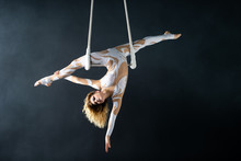 A Young Girl Performs The Acrobatic Elements In The Air Trapeze. Studio Shooting Performances On A Black Background