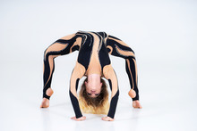 A Young Flexible Girl Performs The Acrobatic Elements On The Floor. Studio Shooting Performances On A White Background