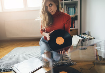 Young woman sitting on floor with vinyl record. Playing music on turntable, leisure time, hobbie