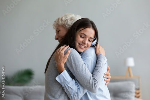 Happy mature mother and grown-up adult daughter hug cuddle share close intimate moment together, smiling elderly mom and millennial girl child embrace make peace reconcile after fight