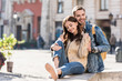 © LIGHTFIELD STUDIOS - Selective focus of boyfriend hugging girl sitting on stone surface and smiling in city