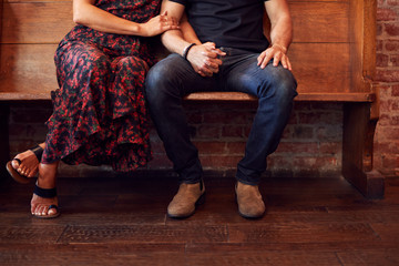 Close Up On Feet Of Same Sex Couple Holding Hands Sitting On Bench Together