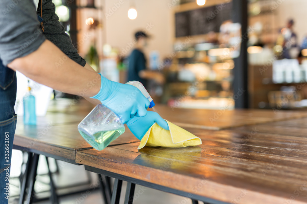 Waiter cleaning the table with disinfectant spray and microfiber cloth in cafe. - obrazy, fototapety, plakaty 
