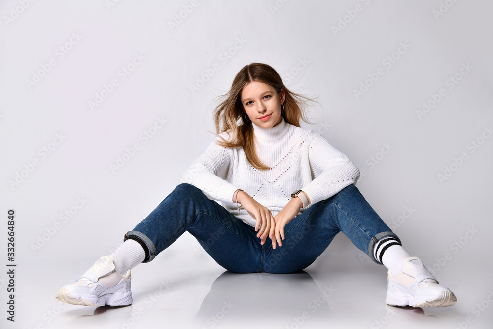 Teenage female in jeans, sweater, socks and sneakers. Smiling, sitting