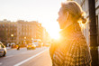 © Polina - An adult woman in the rays of the setting sun stands on the street and looks away.