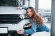 © standret - Positive woman in blue shirt embracing her brand new car. In auto salon