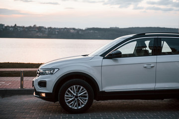 Particle side view of modern white car parked near lake at evening time