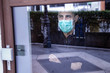 uomo con mascherina guarda il mondo attraverso un vetro non potendo uscire per le restrizione a causa della pandemia