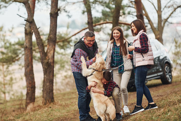 Wall Mural - Happy family have fun with their active dog near modern car outdoors in forest