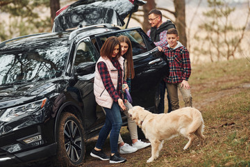 Wall Mural - Happy family have fun with their dog near modern car outdoors in forest