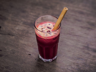 close-up of red healthy beetroot fruit and vegetable juice with ice and bamboo straw on a table