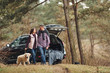 © standret - Happy mature couple have a walk with their dog in autumn or spring forest near modern car