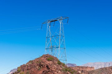 Wall Mural - High voltage transmission tower with parallel lines on the top of the rocky hill in the blue sky